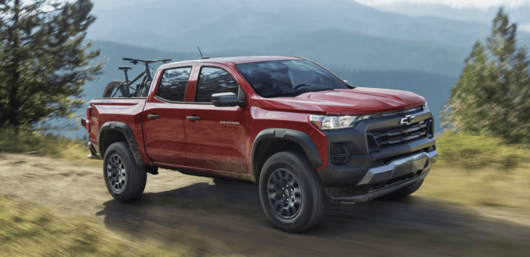 red Chevrolet Colorado driving on dirt road with mountains in the background
